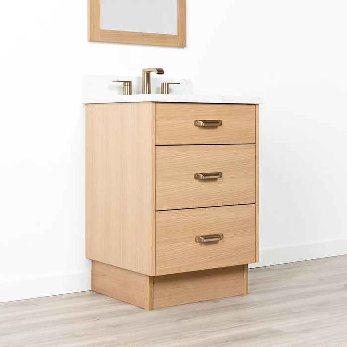 Ashbury 24" White Oak Vanity with Arctic Trace quartz top, toe kick base, and new bronze handle – left-side closed view.